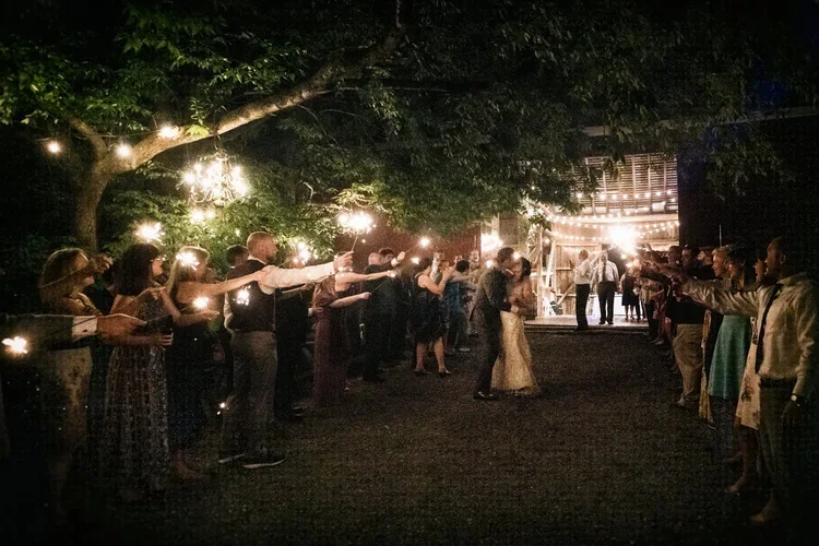 People at an outdoor wedding reception holding sparklers in a line.