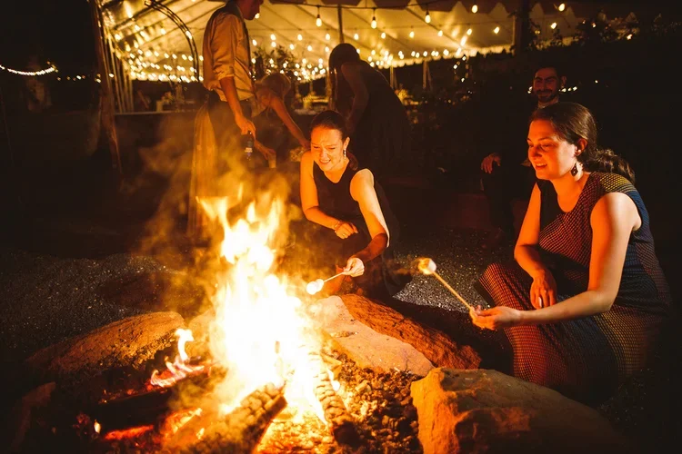 People roasting marshmallows around a campfire at night, under string lights at a private event at Rocklands Farm Winery