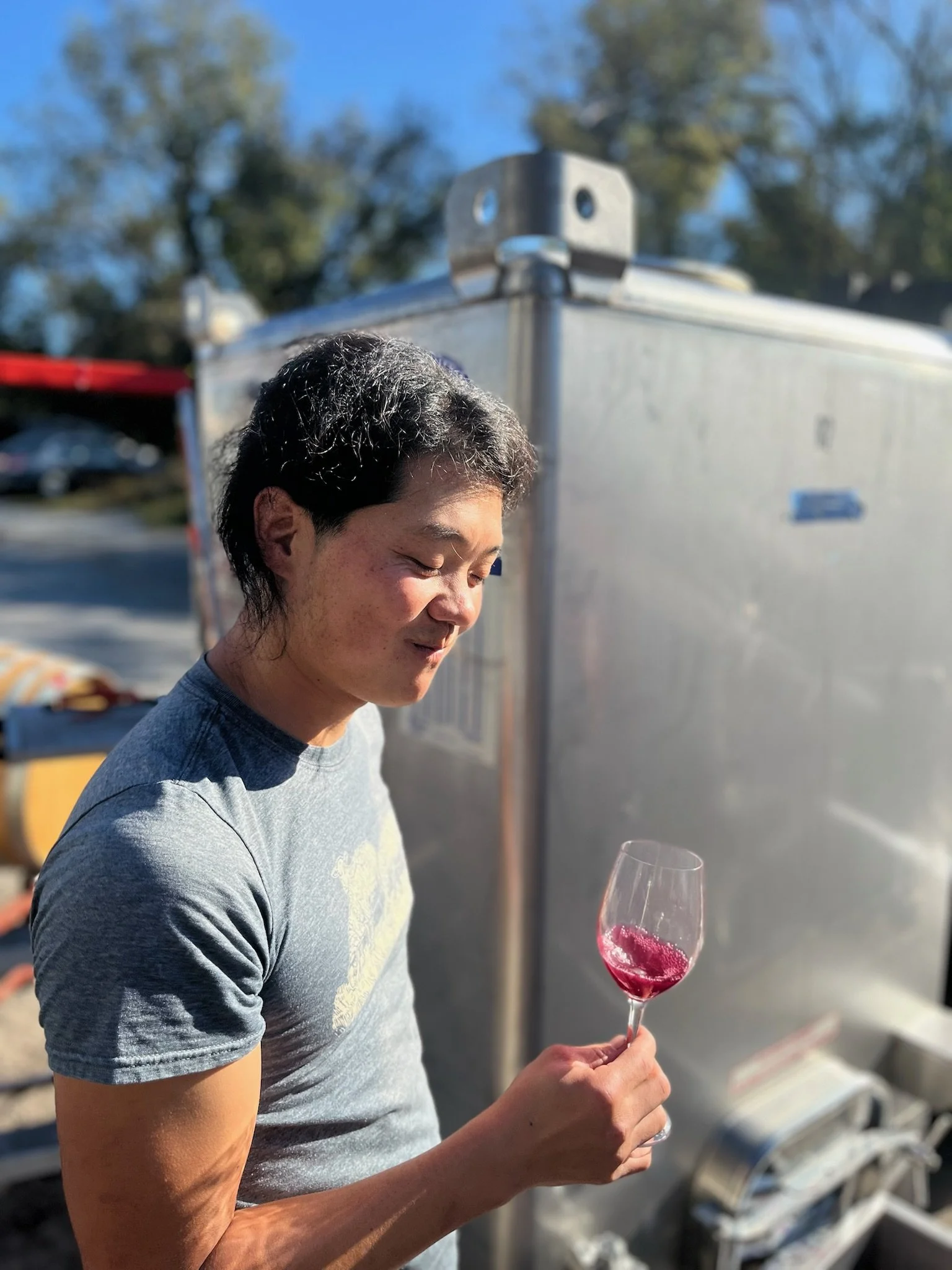 Man smiling while holding a glass of red wine outdoors at Rocklands Farm Winery.