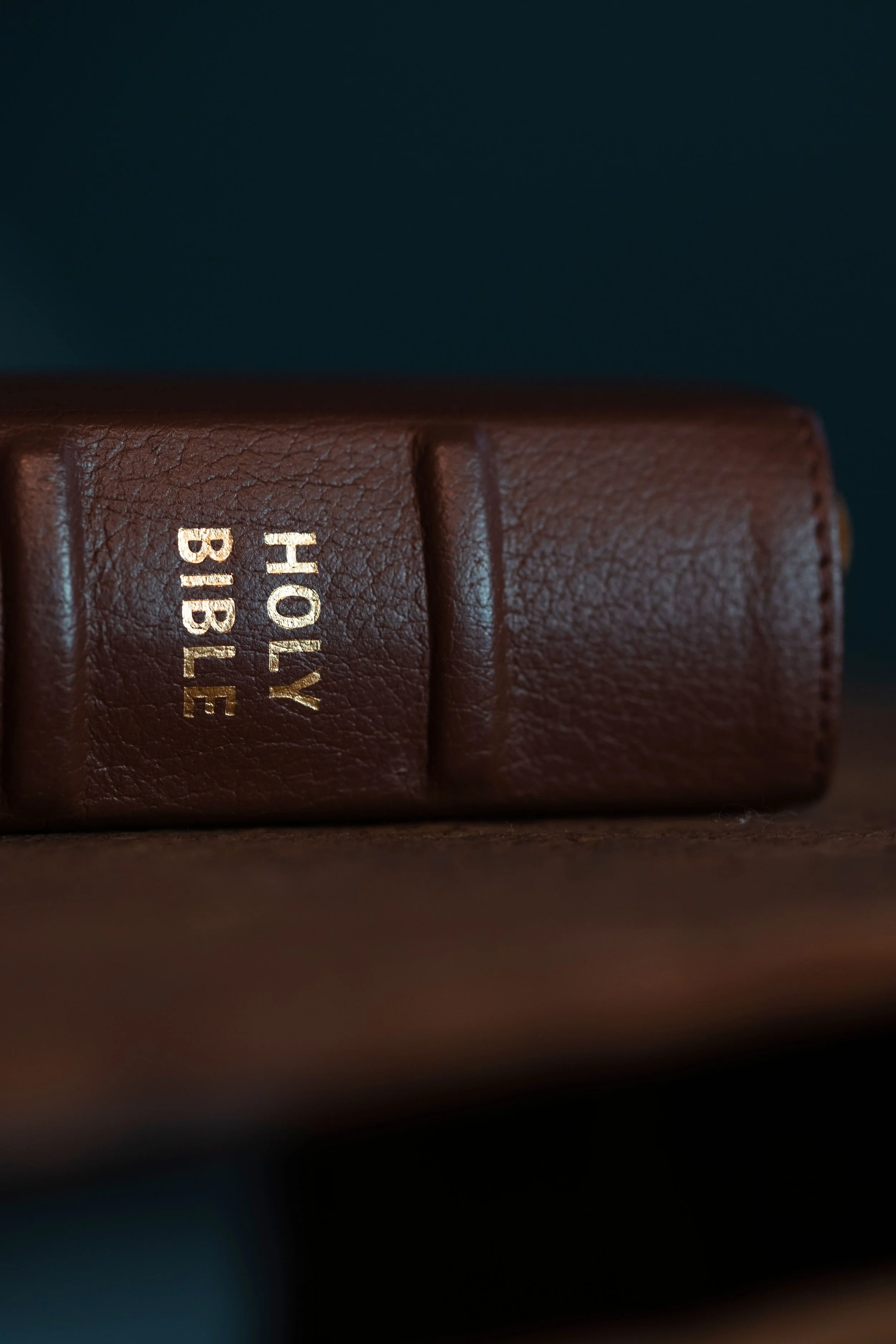 Close-up of a brown leather-bound book titled "Holy Bible" in gold lettering, with a dark background.