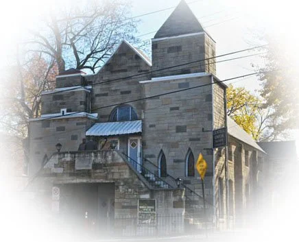 Old stone church with a steeple and stairs leading to the entrance, surrounded by leafless trees.