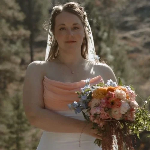 A woman in a wedding dress holding a bouquet of flowers outdoors.