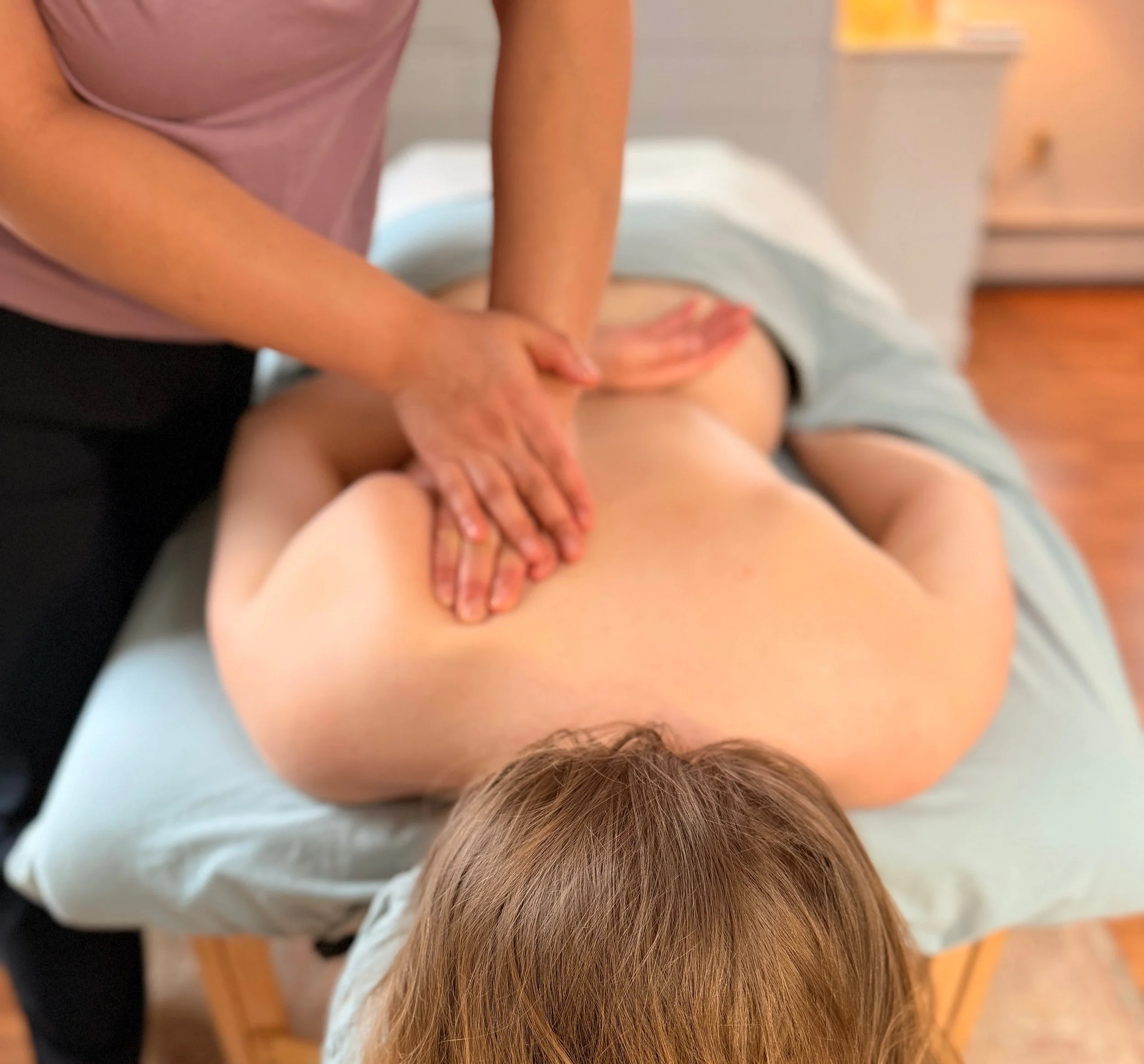 A person performing a massage or physical therapy on another person's back in a room with a wooden floor.
