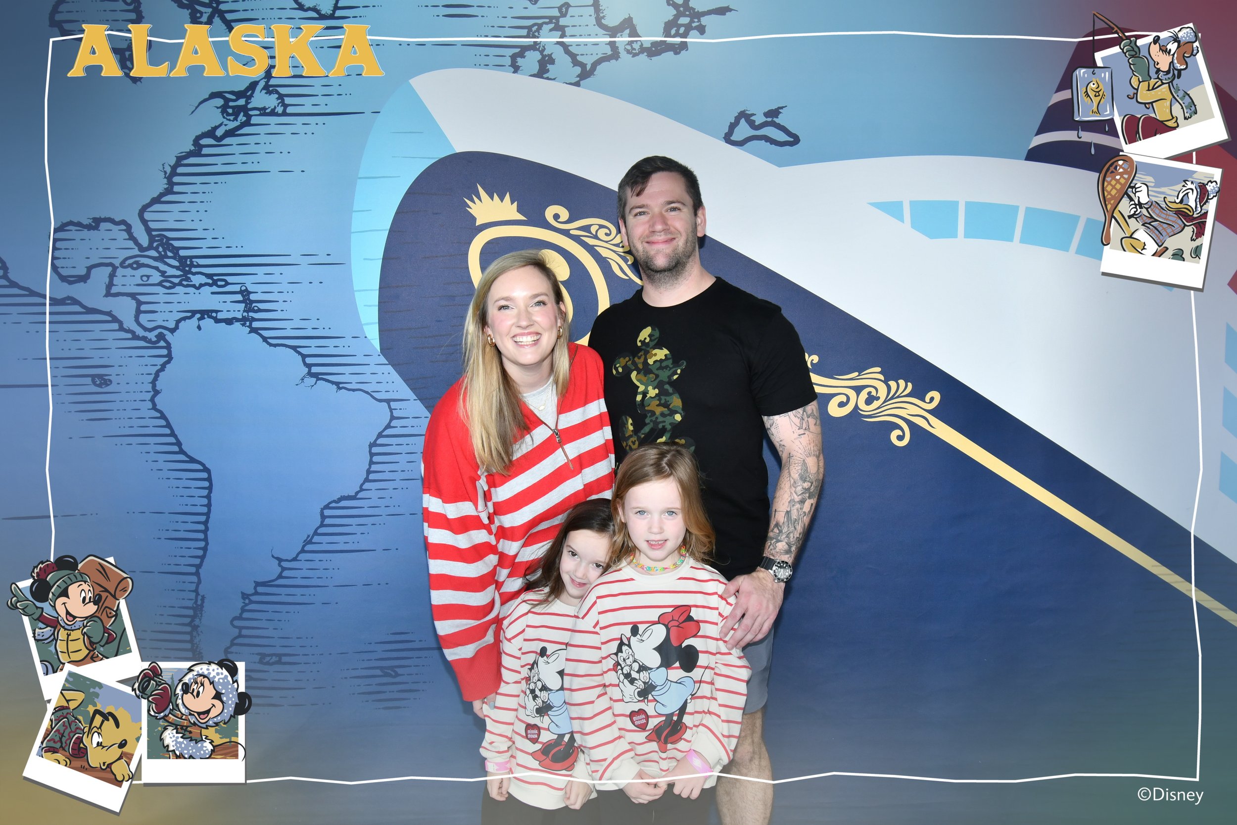 A family of five posing in front of a blue wall with Disney and Alaska themed decorations. The wall features a map outline of Alaska, cartoon images of Disney characters like Mickey Mouse, Minnie Mouse, and Goofy, and photos of Disney characters including Donald Duck and Chip and Dale. The family includes a woman with long blonde hair wearing a red and white striped shirt, a man with tattoos wearing a black T-shirt, and three children also in Disney-themed clothing.