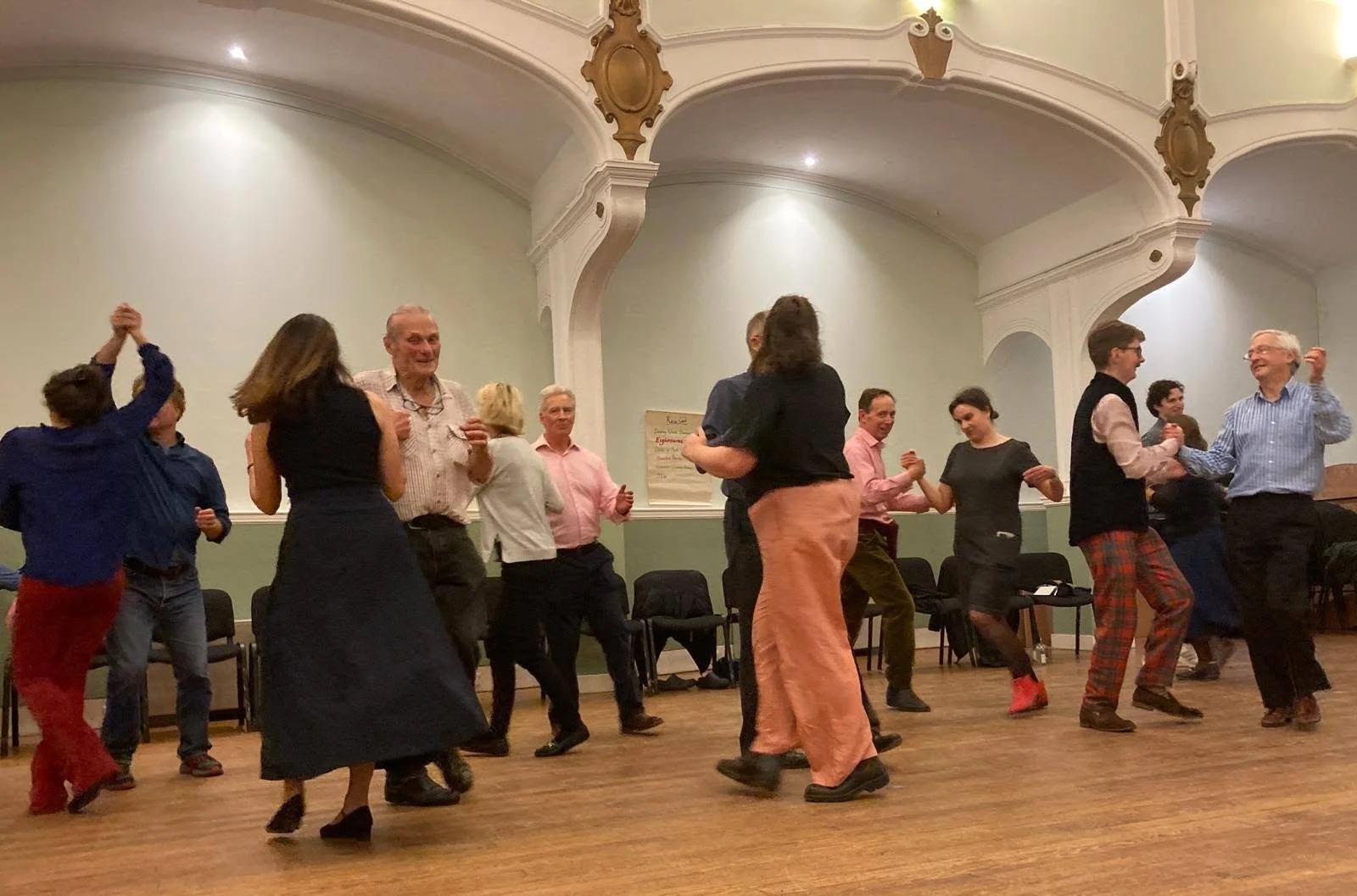 People dancing and socializing in a dance hall with ornate ceiling decor.  Clappy Doo Ceilidh band Scottish Ceilidh band Scottish music traditional scotland music