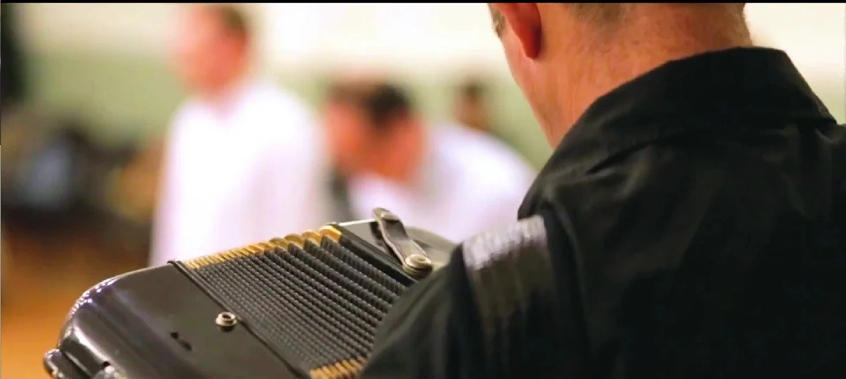 A man playing an accordion in focus with blurred background of people at a social gathering.  Clappy Doo Ceilidh band Scottish Ceilidh band Scottish music