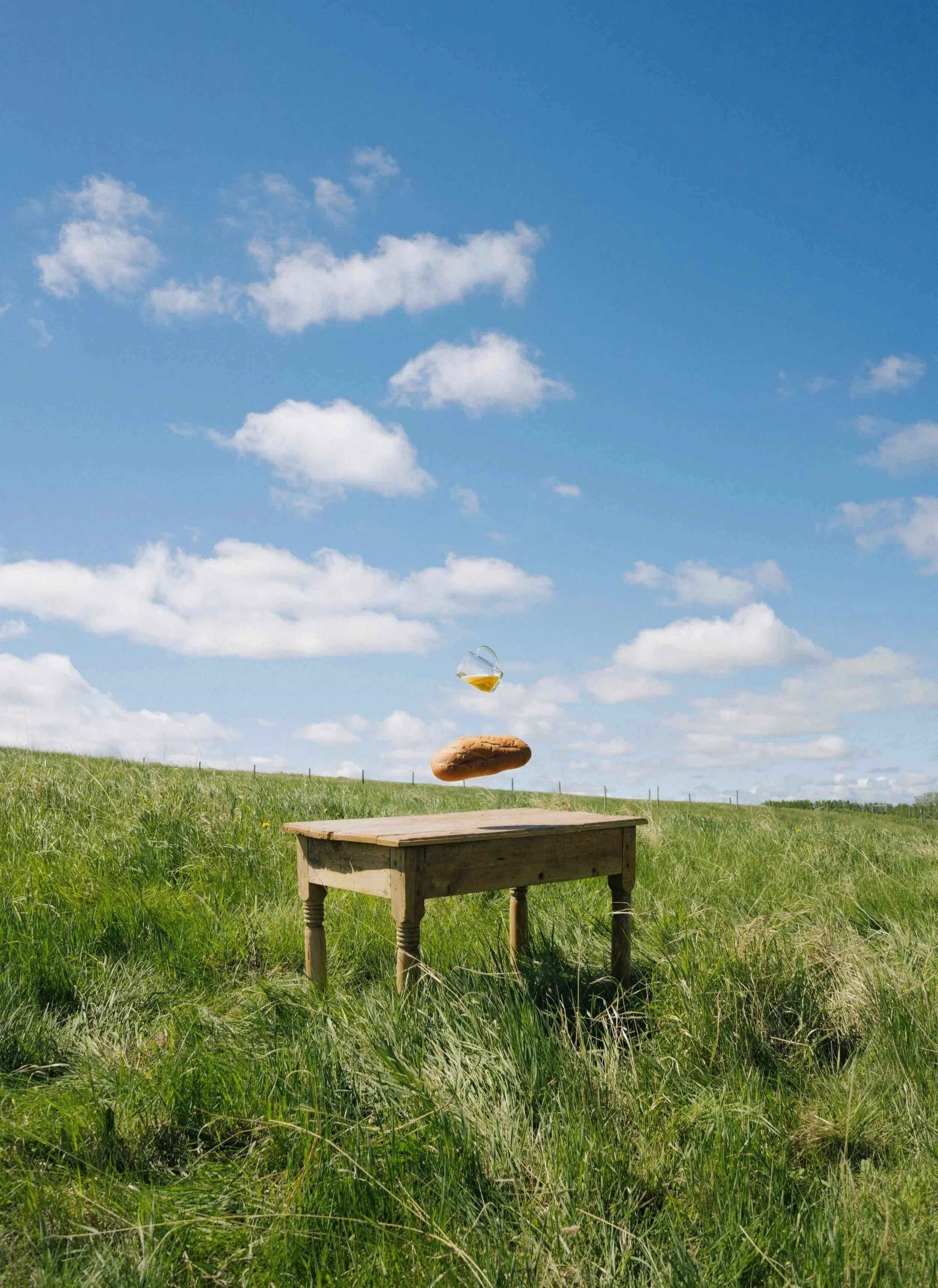 A grassy field with a small wooden table in front of a clear blue sky with a few scattered clouds. Above the table, a mug of Bread Water Beer appears to be floating, with a Loaf below.