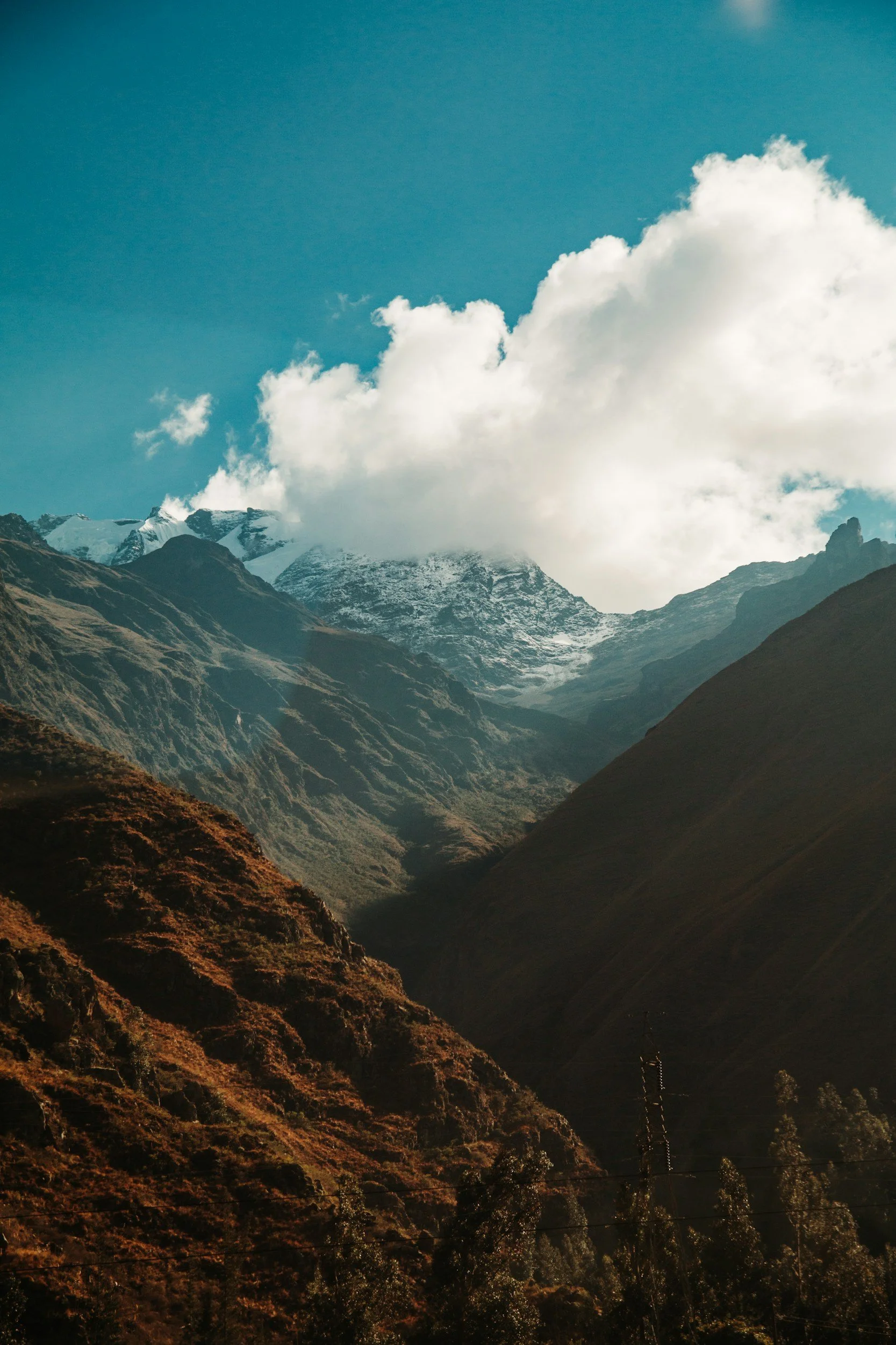 Mountain landscape with snow-capped peaks, green slopes, and a partly cloudy sky.