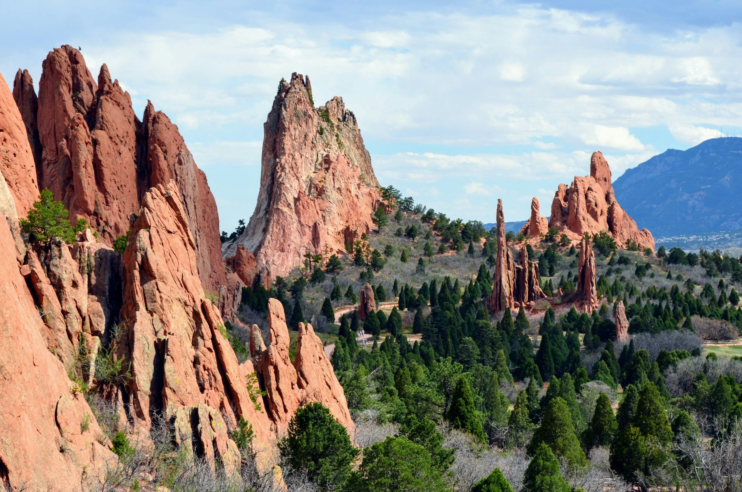 Red rock formations with green trees in a scenic landscape under blue sky with clouds.