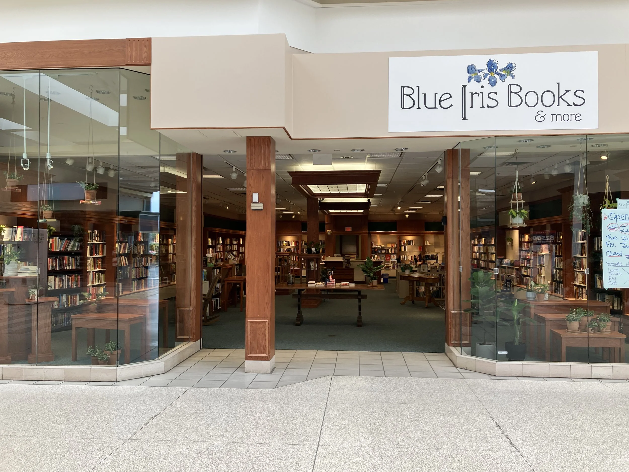 Entrance to a bookstore called Blue Iris Books with glass walls, wooden accents, and bookshelves inside.