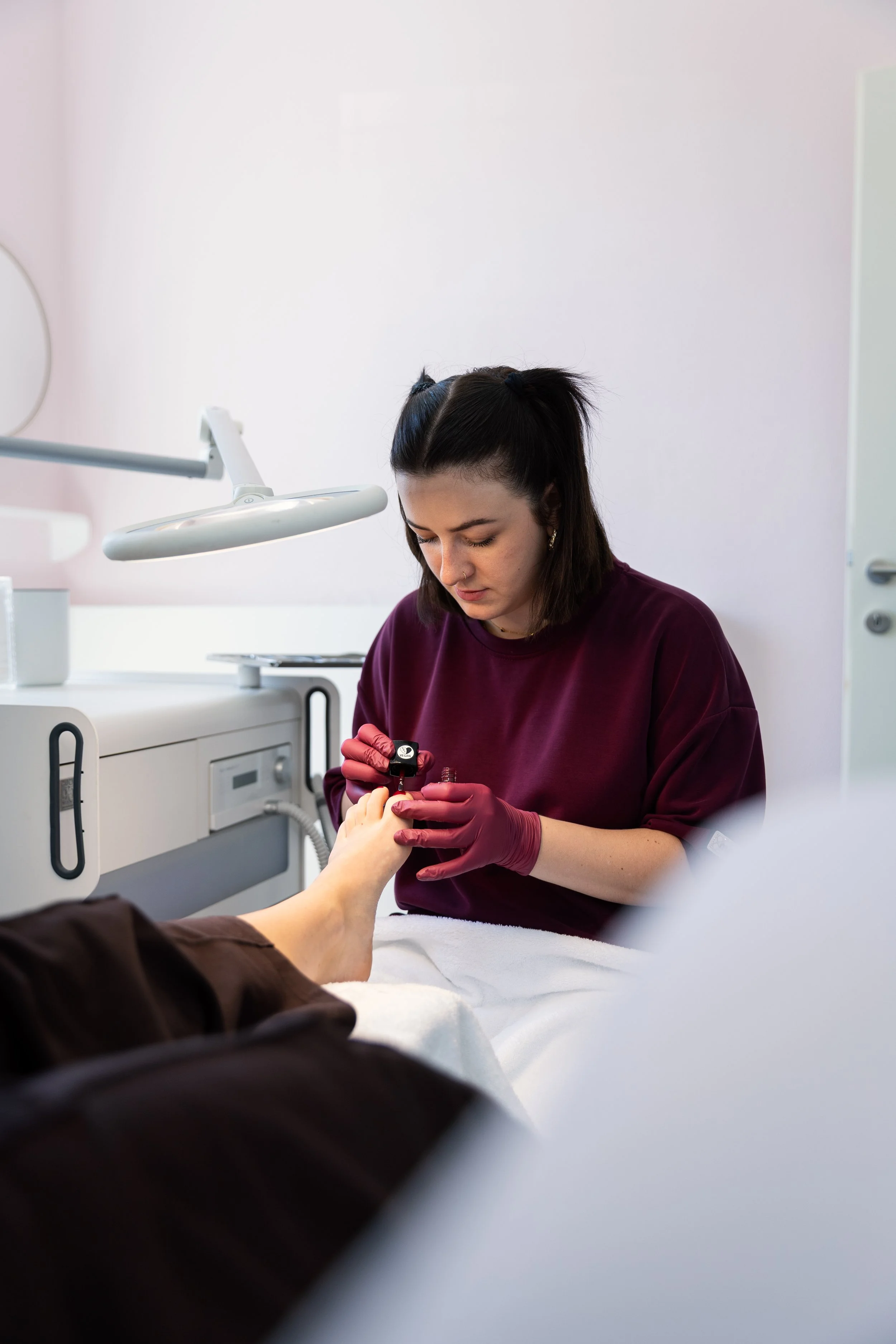 Eine Pflegekraft in Burgunderfarbe untersucht die Hände eines Patienten in einem medizinischen Raum.
