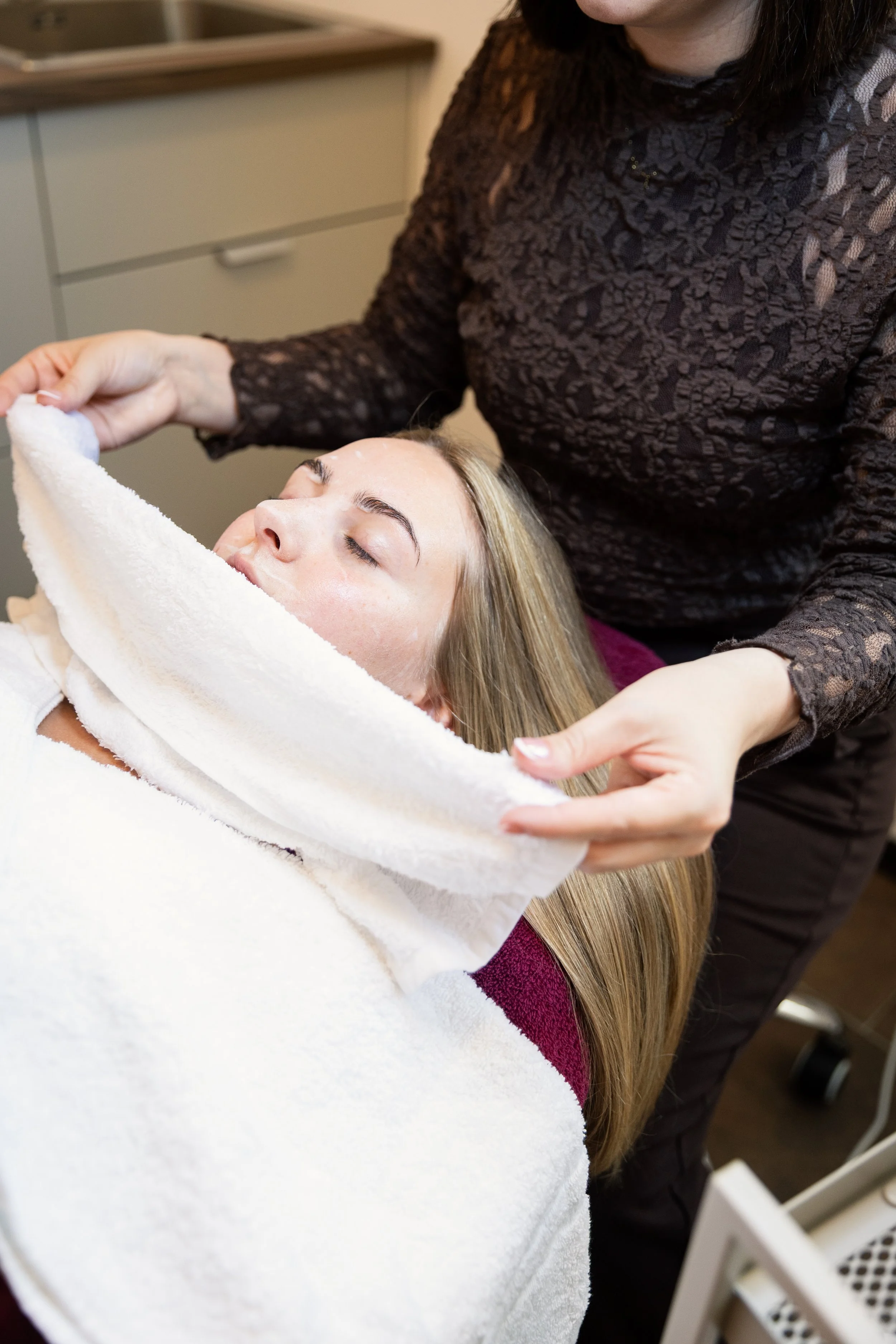 Eine Frau erhält eine Gesichtshautreinigung in einem Kosmetiksalon, während eine Kosmetikerin vor ihr steht.