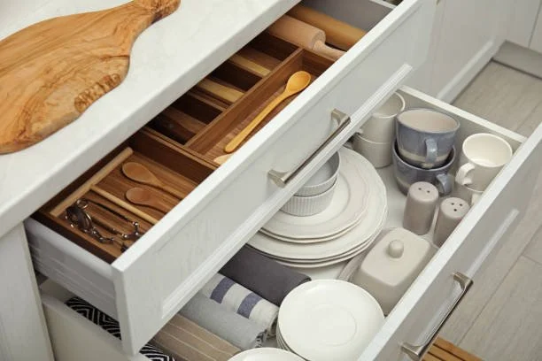 Kitchen drawer containing plates, bowls, cups, salt and pepper shakers, and a striped cloth.