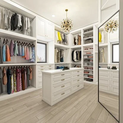 A white walk-in closet with built-in shelves and drawers, organized with clothes, shoes, and accessories. There is a central island with drawers, a large mirror, and two chandeliers hanging from the ceiling.