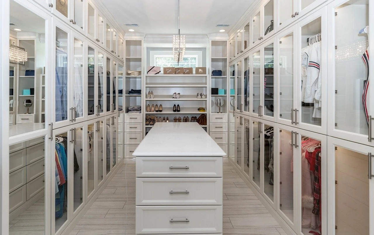Walk-in walk-in closet with white built-in cabinets, glass doors, and an island in the center, containing clothes, shoes, and accessories.