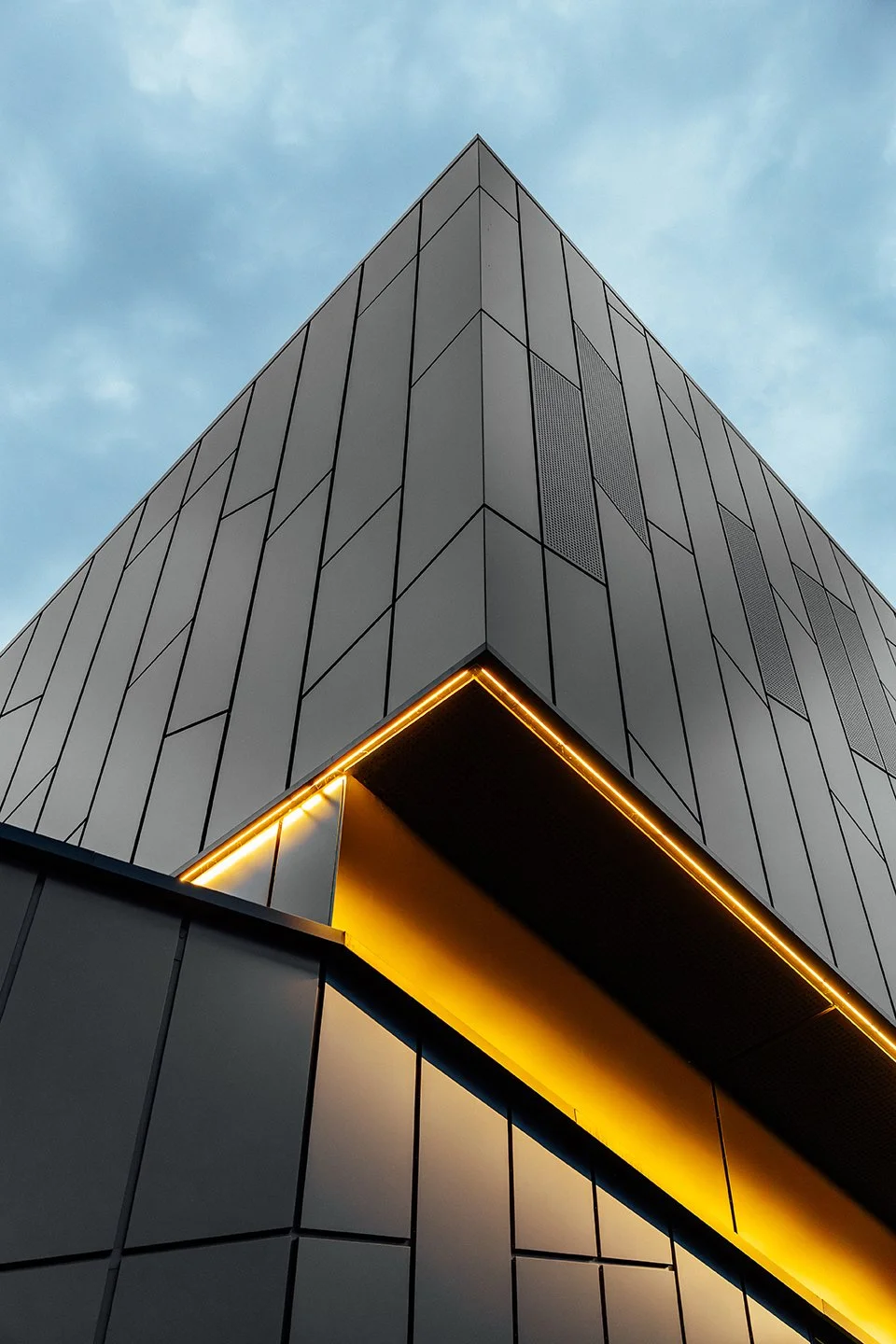 Low-angle view of a modern, geometric building with a neon yellow-lit overhang.
