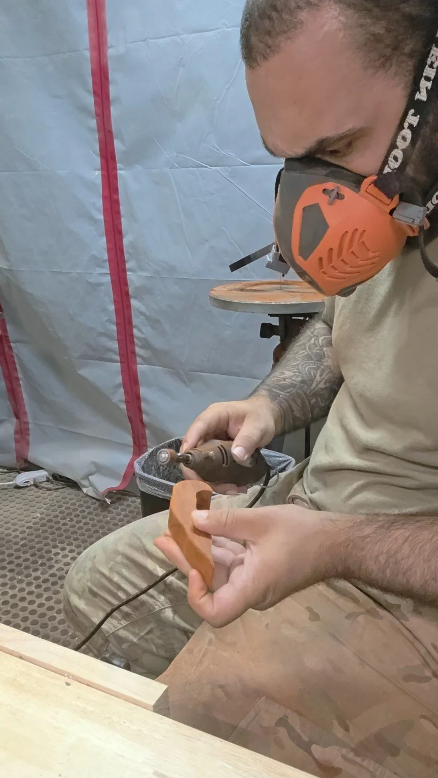 Man using a rotary tool while holding a piece of wood in a workshop.