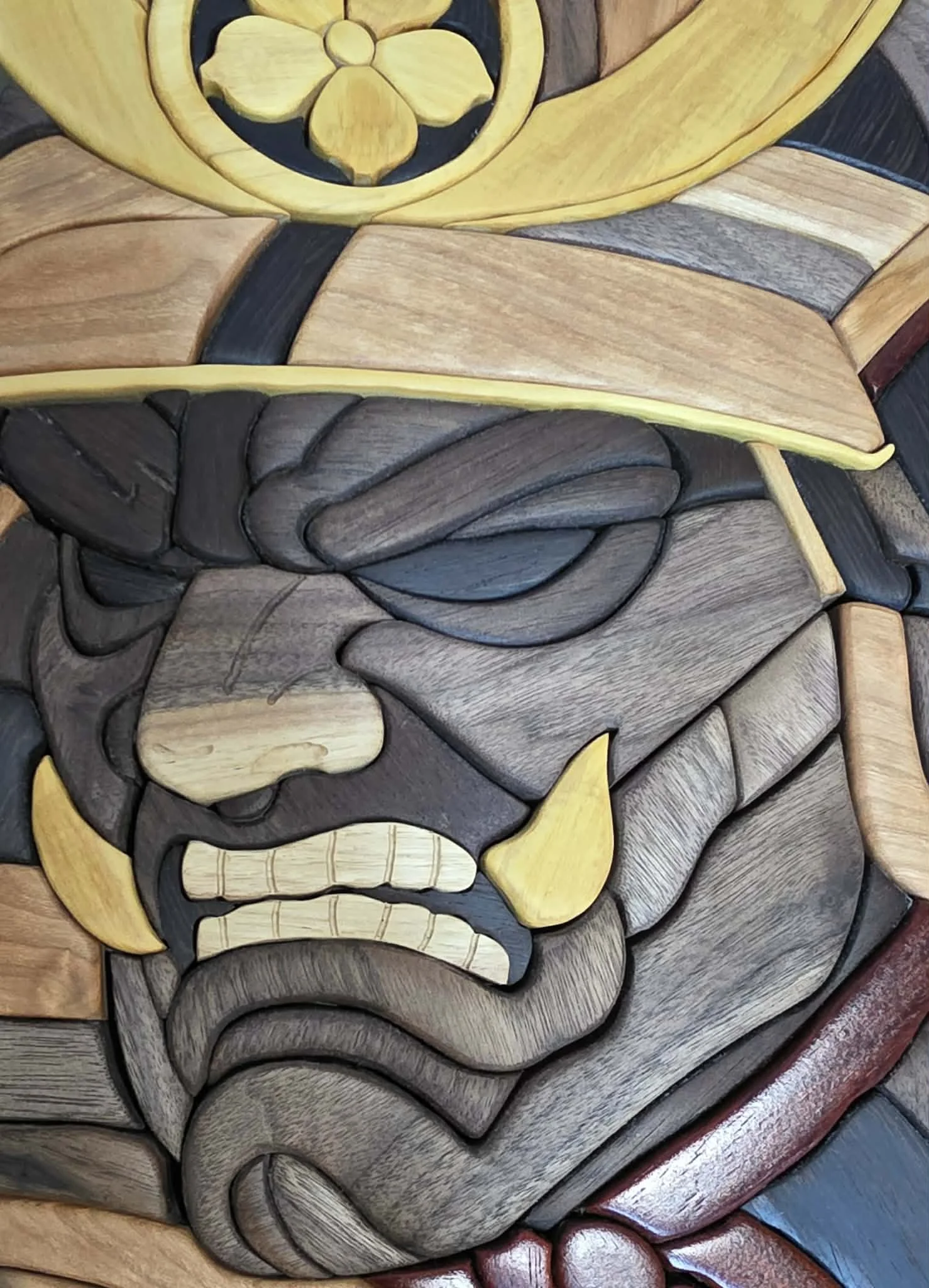 Close-up of hardwood samurai face and helmet showing contrasting natural wood tones and sculpted details.