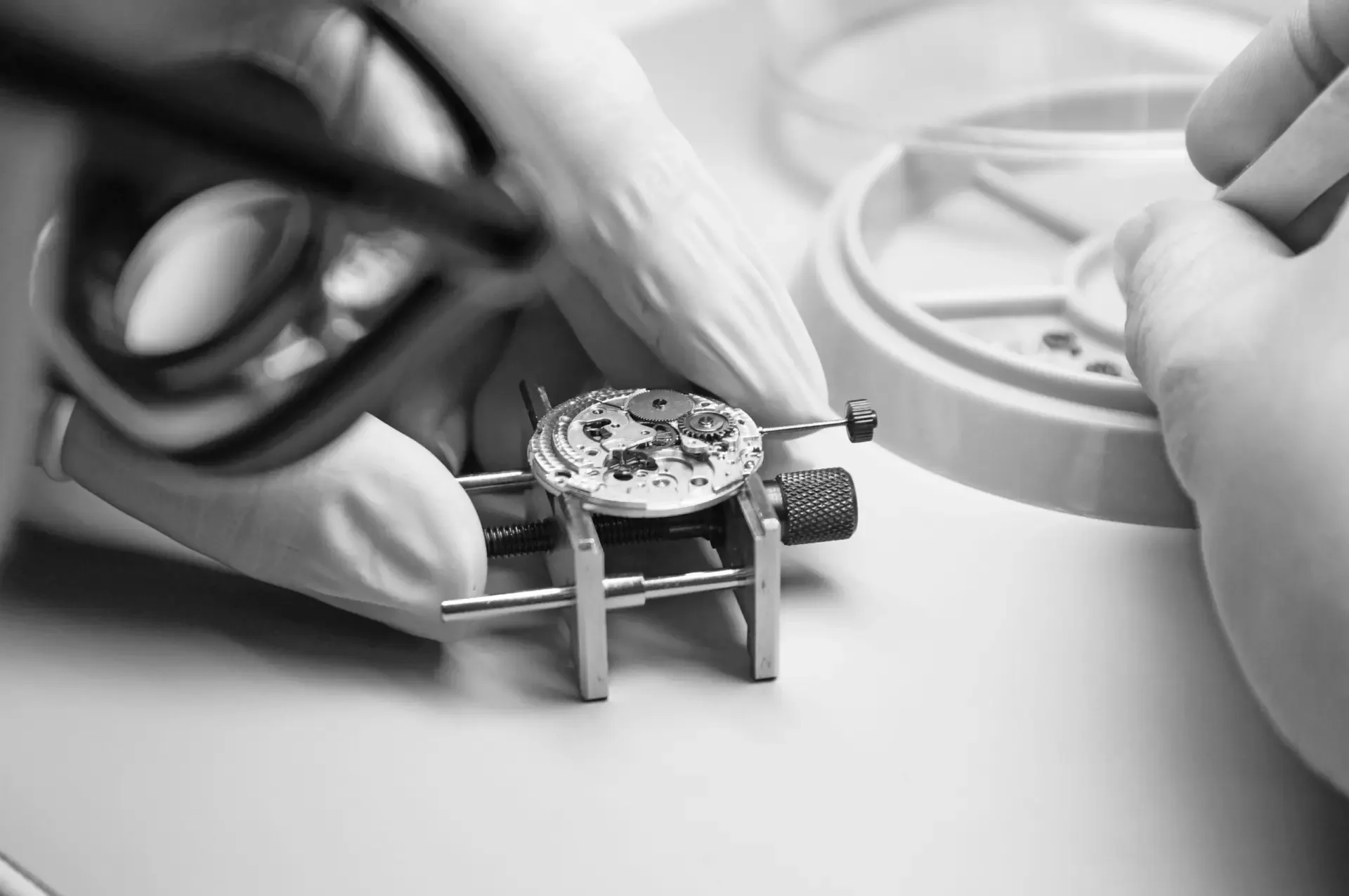 Le mani di una persona che lavora su un movimento di orologio con strumenti di precisione in un ambiente di lavoro.