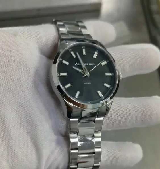 Orologio da polso in acciaio inox con quadrante nero, indici e lancette argentati, indossato su una mano con guanto bianco.