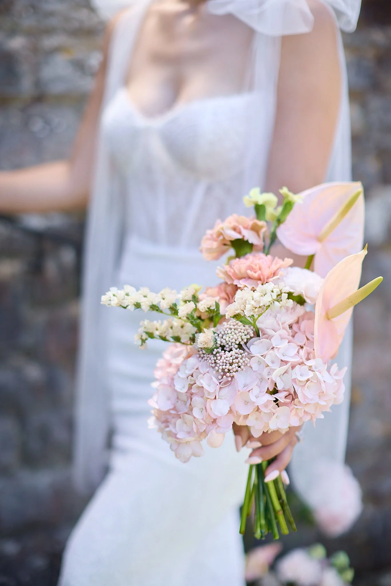 Close-up of a bride holding a bouquet of soft pink and white flowers, with a blurred background.