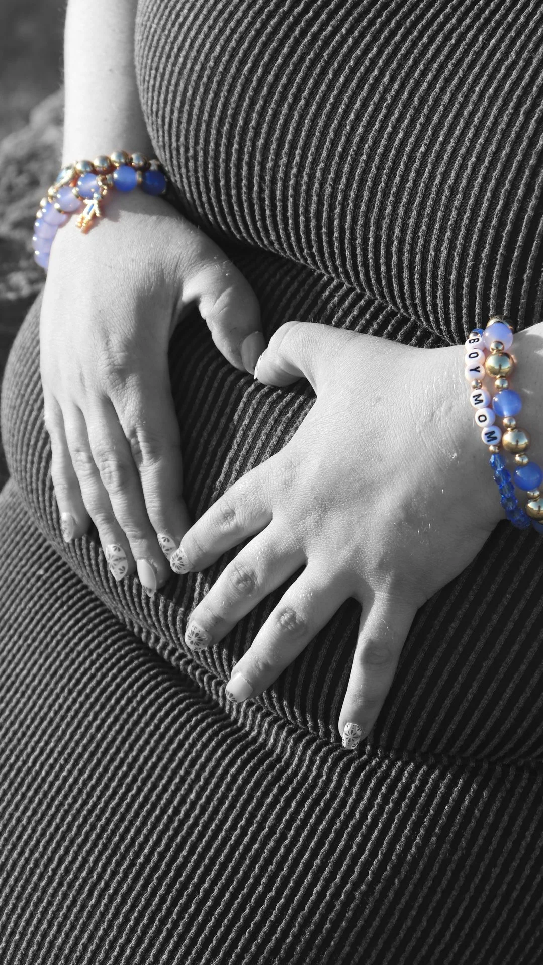 Close-up of a person's hands making a heart shape, wearing bracelets with blue beads and gold accents, against a striped fabric background.