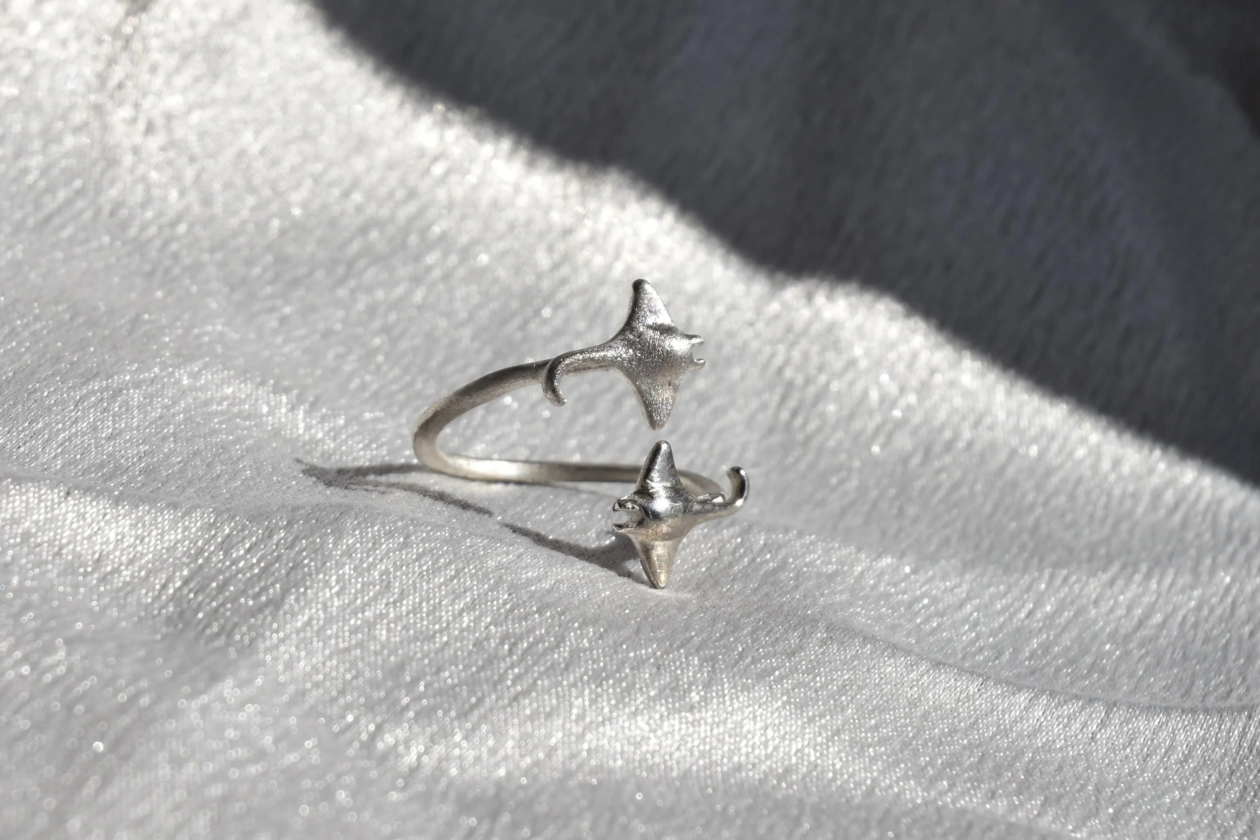 Zilveren ring met stervormige decoratie op een glanzende witte stoffen achtergrond.