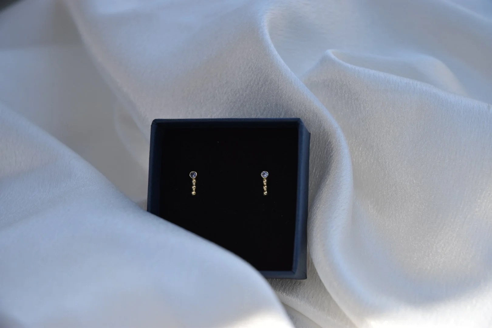 Gouden oorbellen met kleine diamanten in een zwarte sieradendoos op zijden stof.