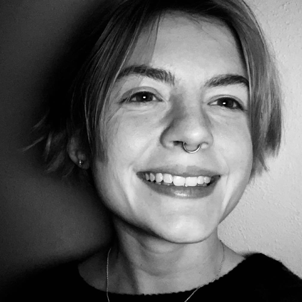 A woman with short hair and piercing in her septum, smiling at the camera in black and white.