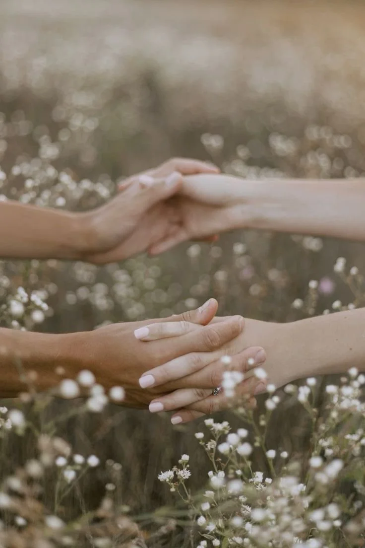 Two people holding hands over a field of small white flowers.