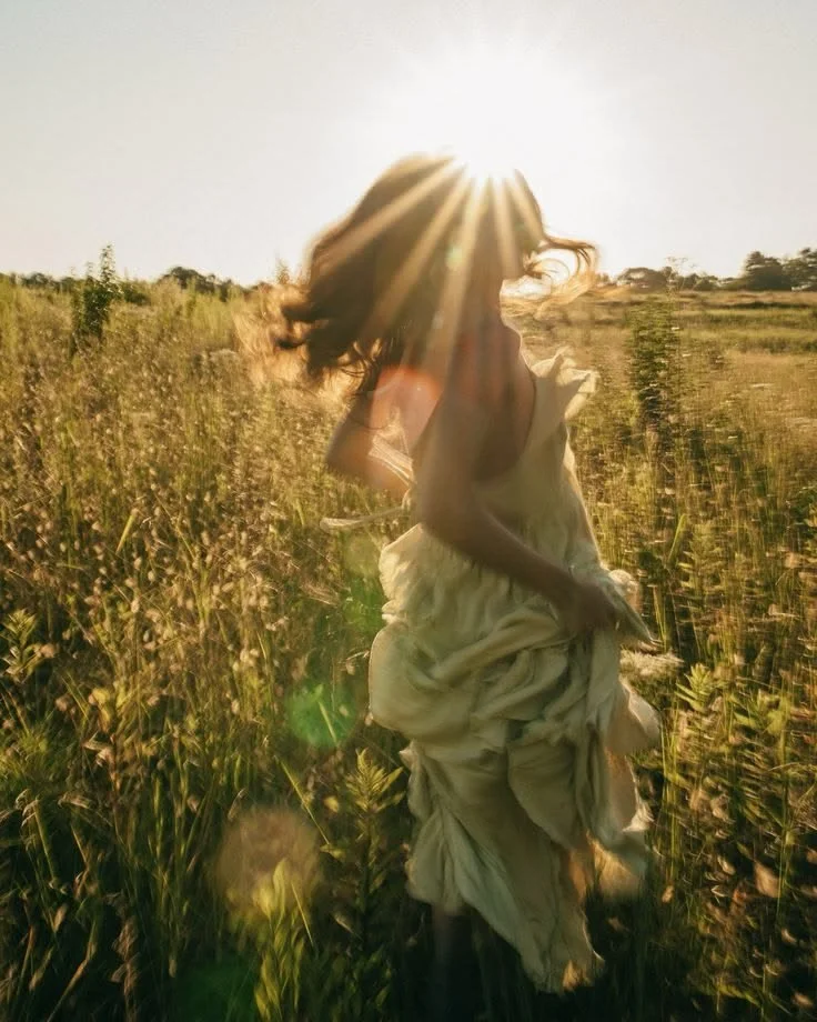 A woman running through a field with the sun behind her.