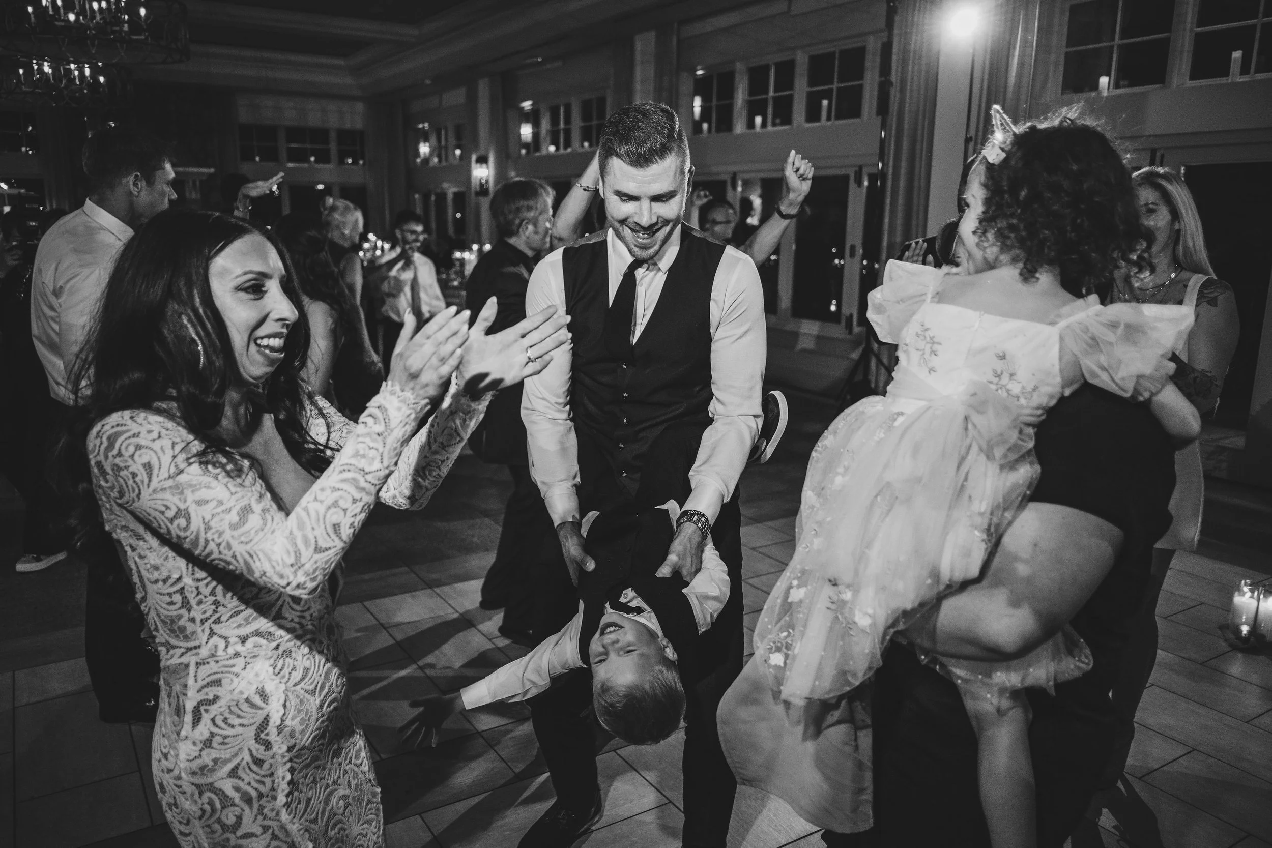 People at a party dancing and celebrating, with some clutching hands or holding each other, in an elegant indoor setting.