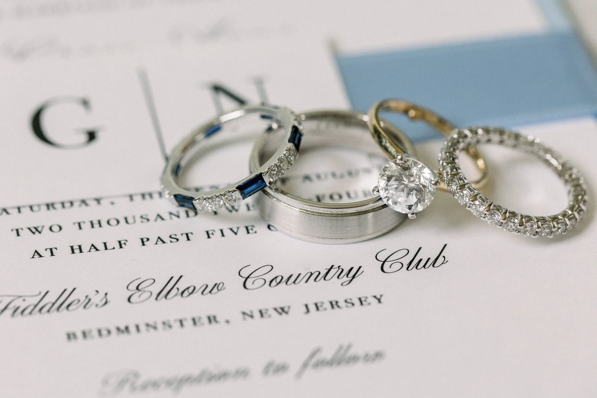 Close-up of wedding rings, including an engagement ring with a large diamond, placed on a wedding invitation with elegant cursive text.