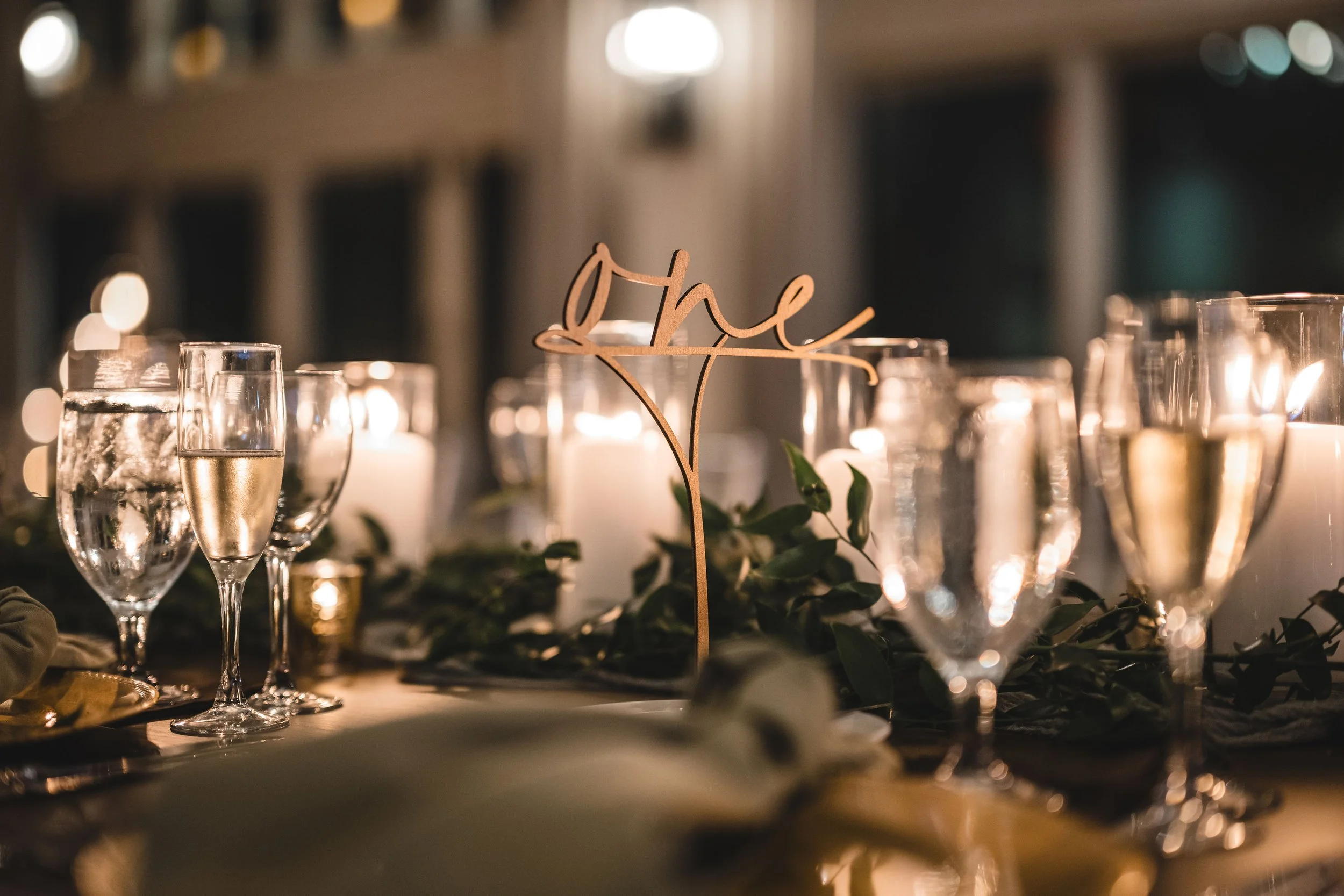 Elegant table setting with champagne glasses, candles, greenery, and a decorative wooden sign that says 'Mr.'