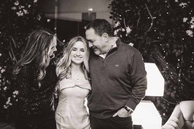 A black and white photo of three people smiling and standing close together, two women and one man, in front of a decorated Christmas tree.