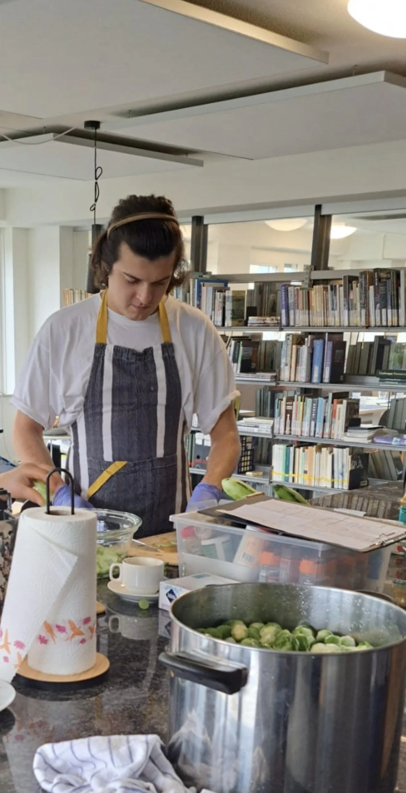 A person (Guillo) preparing food in a kitchen setting, surrounded by shelves of books and various kitchen items.