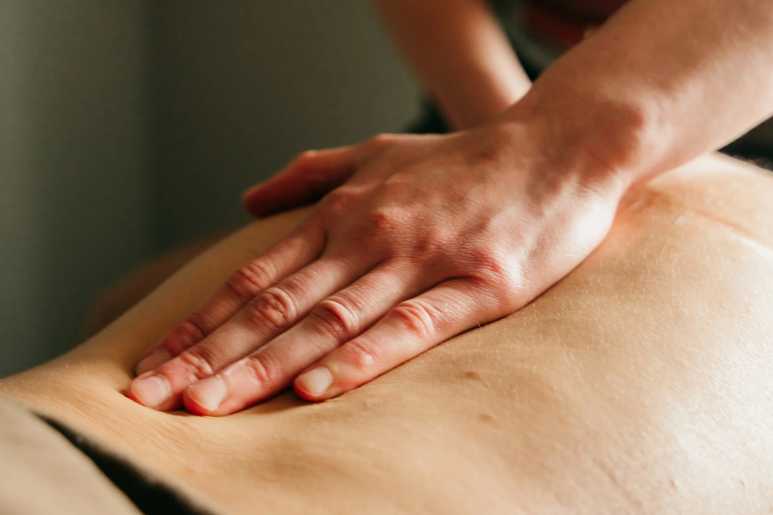 Close-up of a person's back being massaged with hands, showing skin and fingers pressing into the skin.