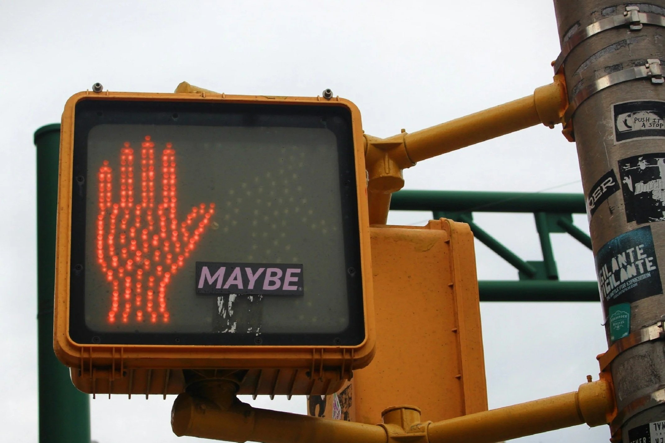 A red illuminated hand stop signal on a yellow traffic signal box at an intersection.