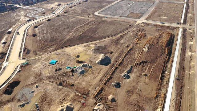 Aerial view of a construction site with dirt, rocks, and incomplete roadways, with some construction vehicles and equipment.