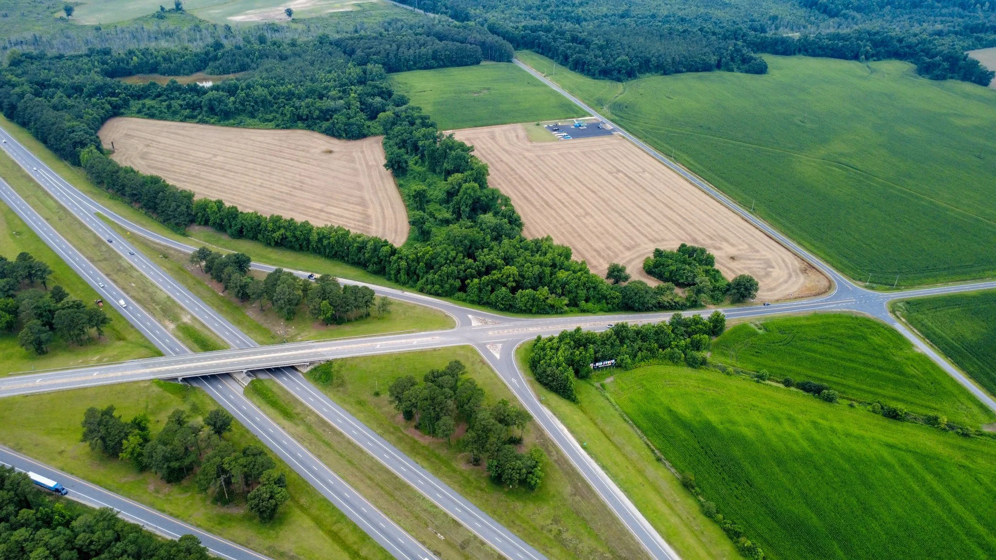 An aerial view of highways intersecting near farmland and lush green fields with trees.
