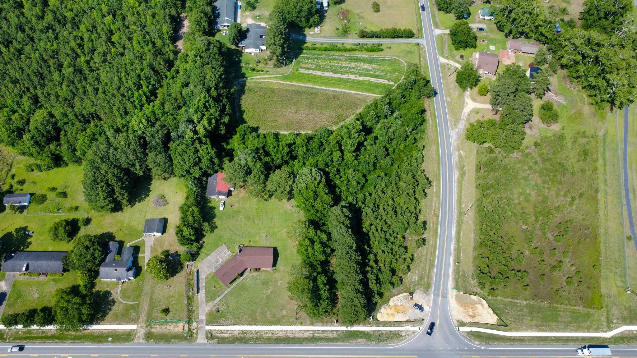 An aerial view of a neighborhood with trees, houses, a road, and a small farm or garden plot.
