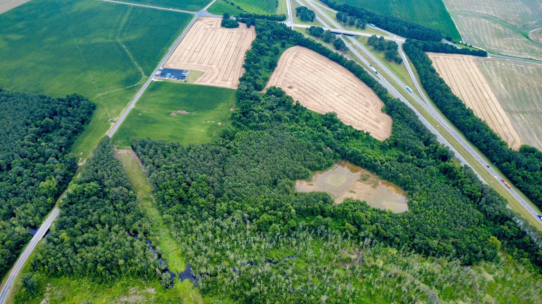 An aerial view of farmland, roads, trees, and a small body of water.