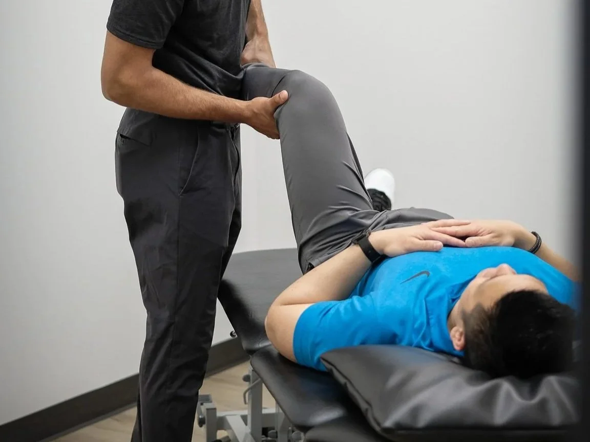 A person lying on a chiropractic examination table with their knees bent, receiving a leg check from a chiropractor.