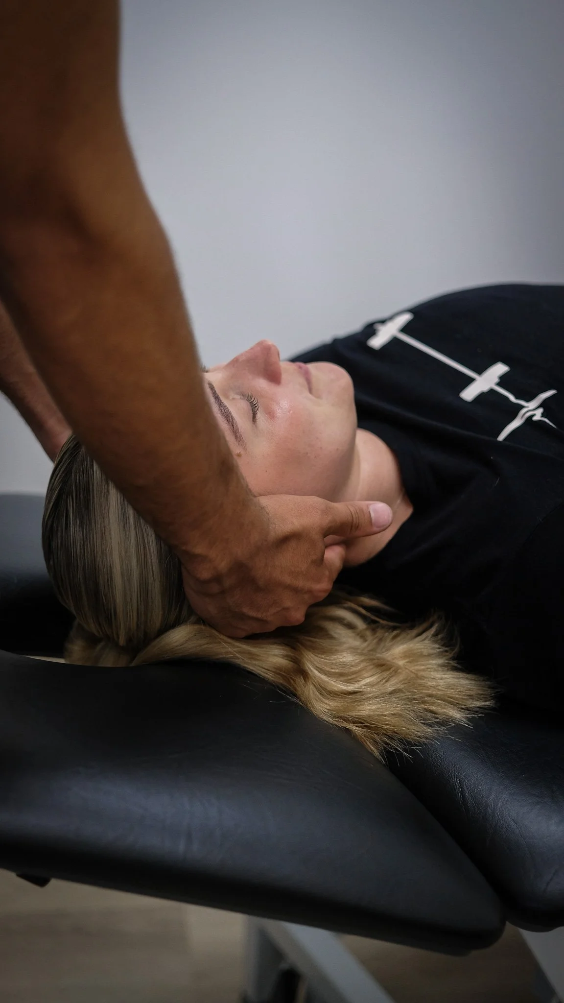 A person lying face up on a chiropractic table while a chiropractor performs manual therapy on a persons neck.