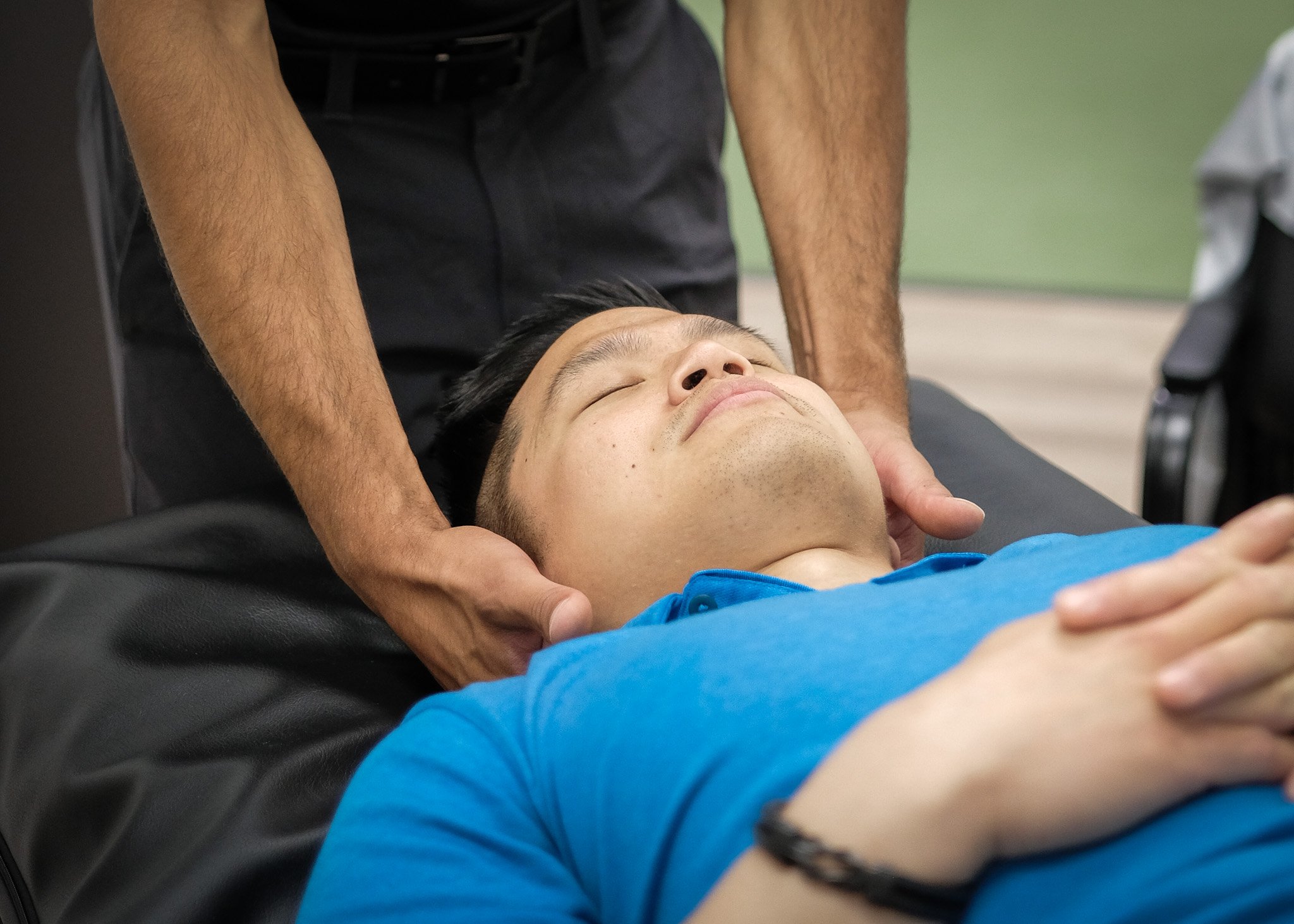 Person lying on a massage table with eyes closed, receiving chiropractic neck manual therapy, with green turf background.