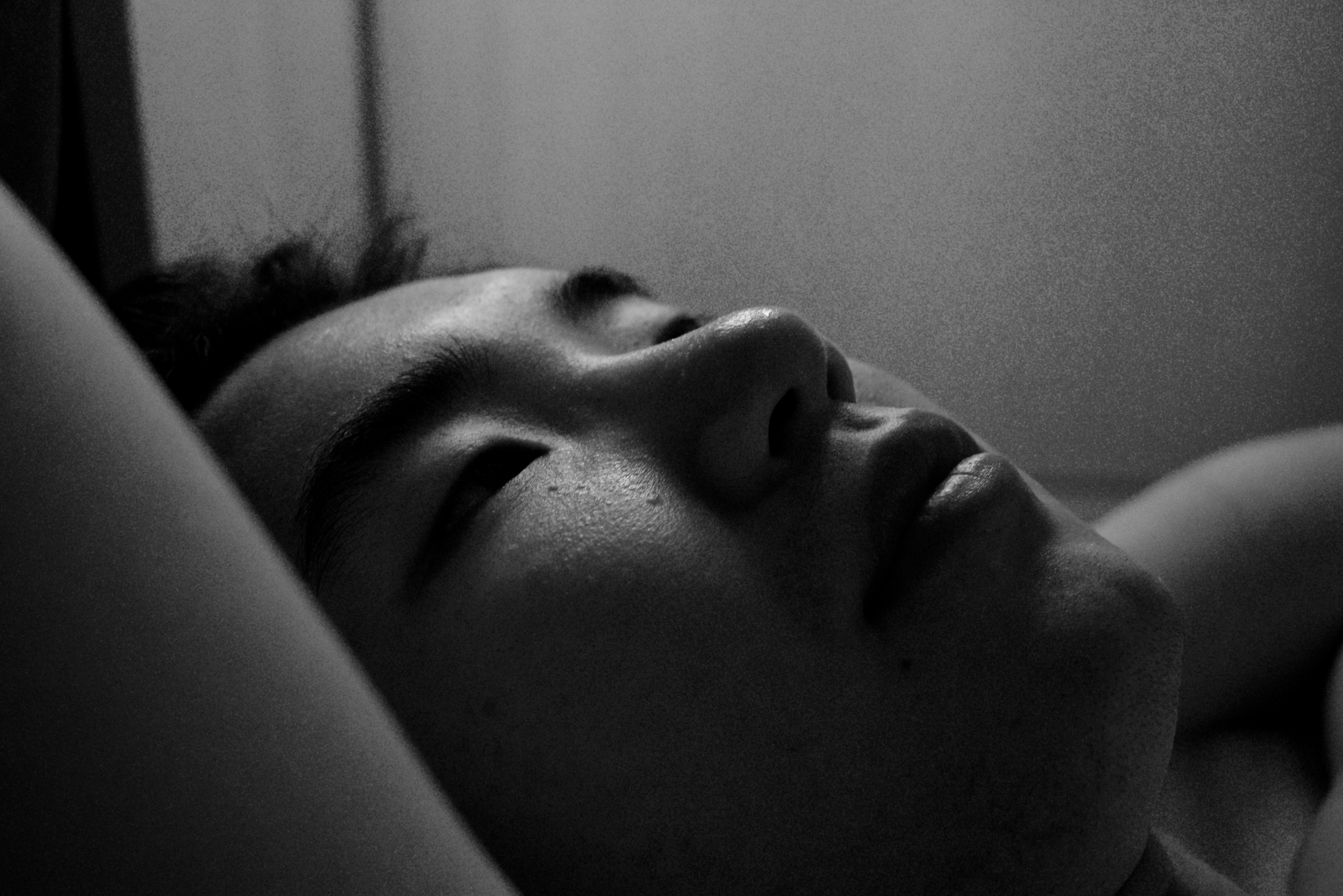 Close-up of a person's face lying down with eyes closed, in black and white.