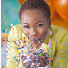 Photographer smiling while blowing colourful confetti towards the camera.