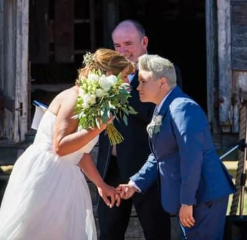 Celebrant standing with a couple during an outdoor wedding ceremony.