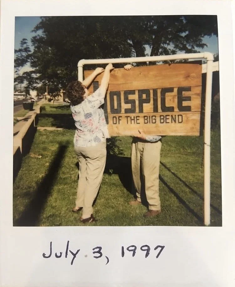 A woman and a person holding a large wooden sign that reads "Hospice of the Big Bend" outdoors in a park-like area with grass, trees, and a sidewalk, dated July 3, 1997.