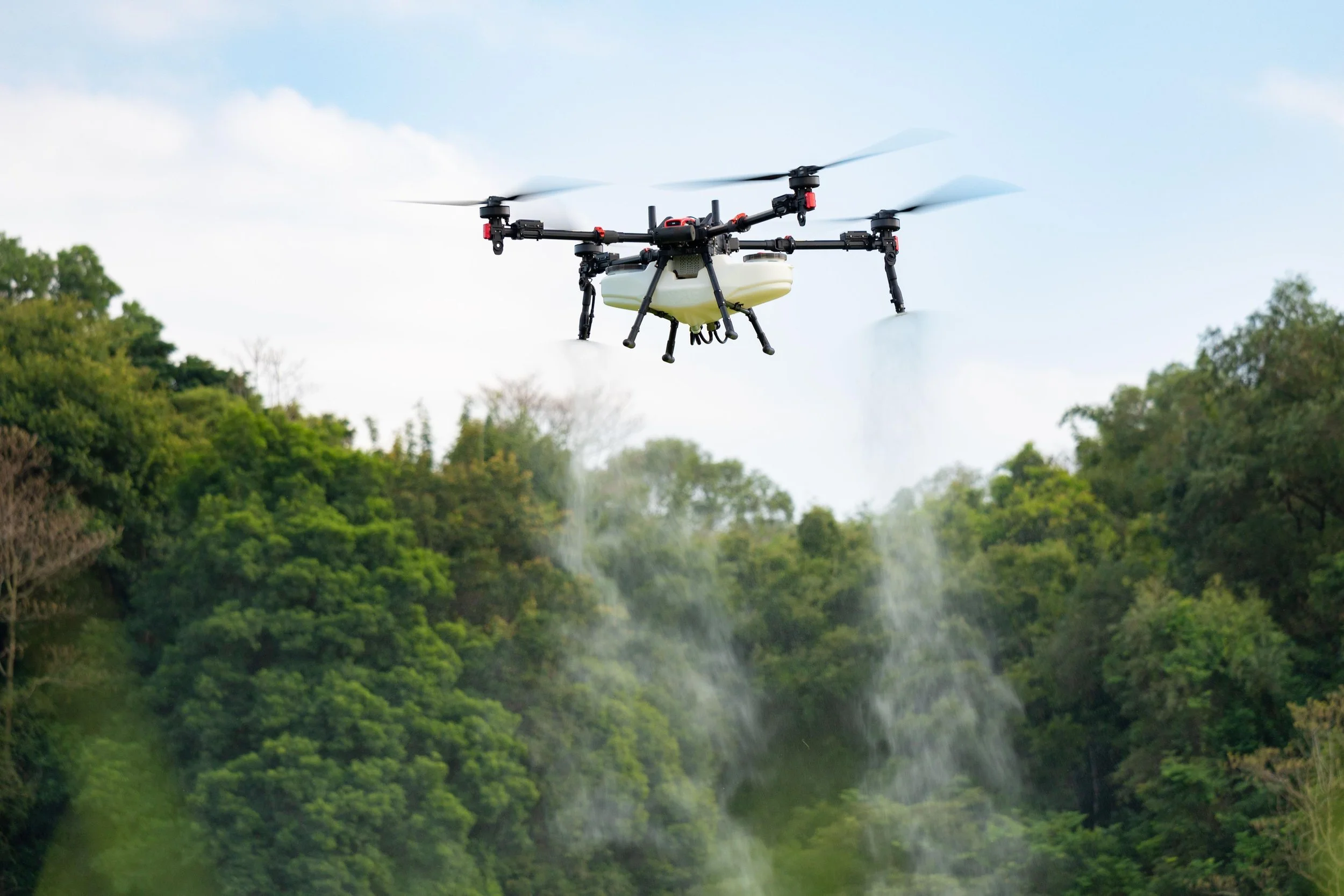 A drone flying above a lush green forested area with a partly cloudy sky in the background.